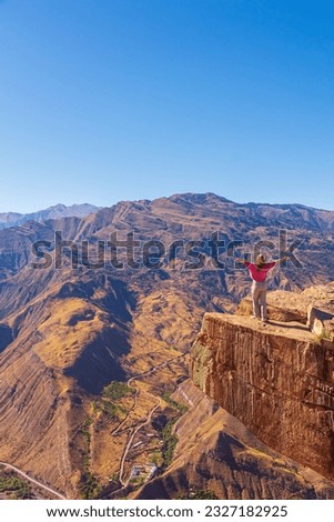 Girl tourist on an extreme ledge in the rock Troll tongue. View of the Caucasus Range, Dagestan.