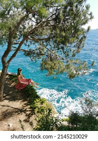 Girl tourist sits in a pine forest on the rocks on a background of beautiful seascape. Mediterranean Sea in Turkey, Kusadasi. Summer background