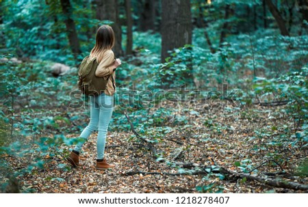 Girl tourist walks in brown boots with a backpack through the woods. On the ground are orange fallen leaves. On the street is autumn.