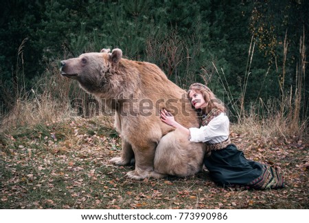 A girl in the traditional Russian dress hugging a real brown big bear in the picturesque forest 
