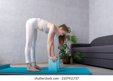 Girl trains flexibility and stretching at home using yoga bricks. Young woman practices yoga with blocks. Uttanasana.