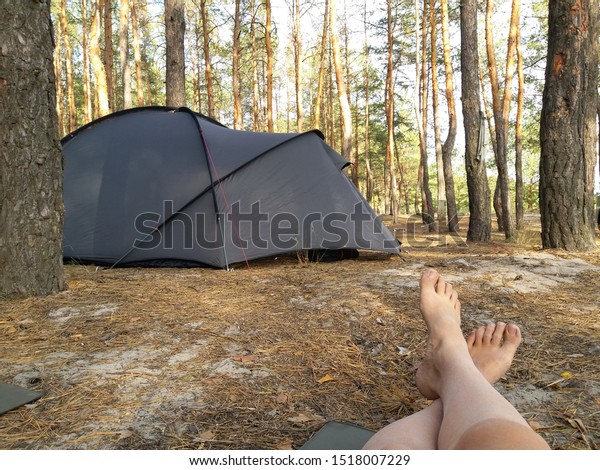 Girl traveler\
in the forest resting lying on a Karimat. Selfie of female legs at\
a campsite in a coniferous\
forest.