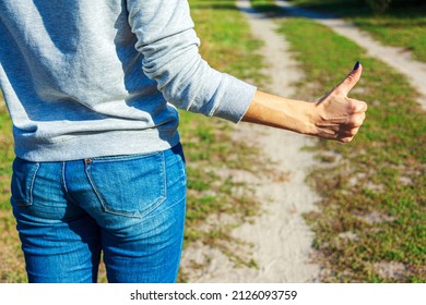 Girl traveler on a rural road showing thumbs up - a hitchhiking sign on the road to stop the car to continue the journey. Female hand with white skin shows thumb up, hitchhiking symbol.