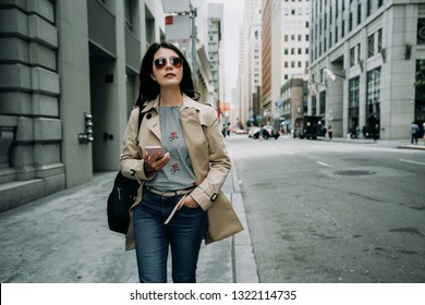 girl traveler in sunglasses walking on street in busy business area with skyscraper building surrounding. young office lady holding cellphone going to work in morning san francisco lifestyle concept.