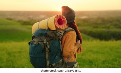 Girl traveler travels along top of green hill in sun, meditation, ecotourism, hike. An active young caucasian woman with backpack goes on hike. Free woman traveler walking through the meadow in summer