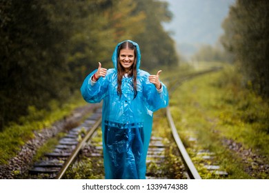 Girl Traveller Wearing Blue Jacket And Go By Forest Railway. Autumn And Raining Season With Dark Green Tones While Girl In Blue Rain Jacket Walks In Forest, Fog, Rain And Clouds