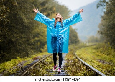 Girl Traveller Wearing Blue Jacket And Go By Forest Railway. Autumn And Raining Season With Dark Green Tones While Girl In Blue Rain Jacket Walks In Forest, Fog, Rain And Clouds