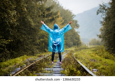 Girl Traveller Wearing Blue Jacket And Go By Forest Railway. Autumn And Raining Season With Dark Green Tones While Girl In Blue Rain Jacket Walks In Forest, Fog, Rain And Clouds