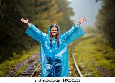 Girl Traveller Wearing Blue Jacket And Go By Forest Railway. Autumn And Raining Season With Dark Green Tones While Girl In Blue Rain Jacket Walks In Forest, Fog, Rain And Clouds