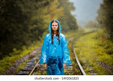 Girl Traveller Wearing Blue Jacket And Go By Forest Railway. Autumn And Raining Season With Dark Green Tones While Girl In Blue Rain Jacket Walks In Forest, Fog, Rain And Clouds