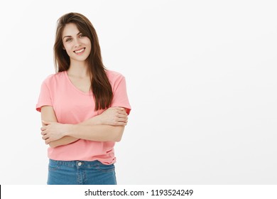 Girl Trying To Control Emotions. Portrait Of Charming Timid Female European In Pink T-shirt, Hugging Herself And Smiling Broadly, Feeling Shy And Unsure While Talking With Stranger In Office