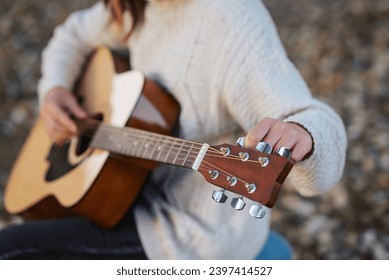 Girl tune acoustic guitar. Close up of hands of a musician tuning guitar outdoor in autumn park