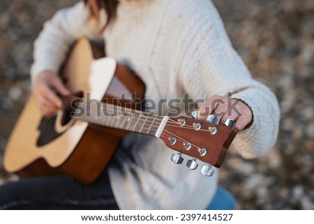 Girl tune acoustic guitar. Close up of hands of a musician tuning guitar outdoor in autumn park