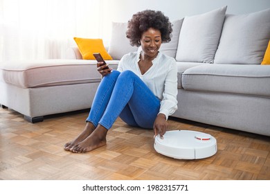 Girl turning on robot vacuum cleaner. Young woman relaxing while robot vacuum cleaning the floor. Woman turns on smart robot vacuum cleaner.