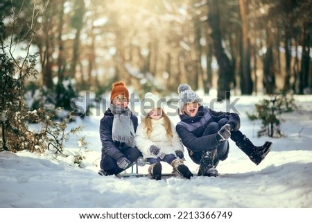 A girl and two boys are playing in the winter forest and sledding. Brothers and sister sledding in the winter park. Children play in the snow with sleds.