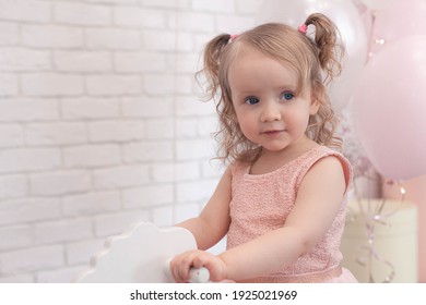 girl of two years old in pink dress sits on a wooden horse