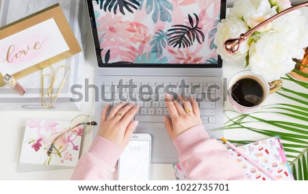 Girl typing on laptop in bright colourful office with pink and chic accessories