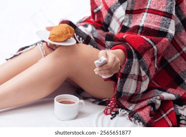 A girl under a red blanket in a warm bed has breakfast with a croissant and coffee. - Powered by Shutterstock