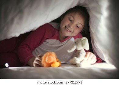 Girl under sheet playing with toys using flashlight, happy and smile
