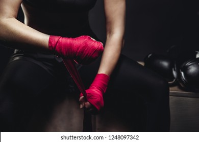 Girl In Uniform On Black Background Is Preparing For Tough Fight, Wraps His Hands Sports Protective Bandages Red And Pink, Lying Next To Boxing Gloves