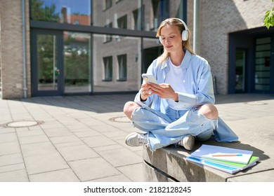 Girl university student wearing headphones using smartphone app sitting on stairs outdoors online learning, remote studying virtual class, watching webinar distance course or listening podcast. - Shutterstock ID 2182128245