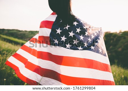 Girl with USA flag walks across the green field.
