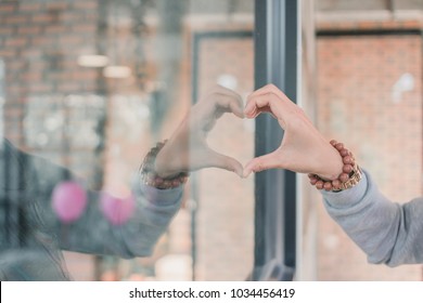 The girl used her hand to make a heart symbol on the surface of the glass in a coffee shop while she went to sit and drink coffee in the morning to show the symbol of love, friendship and compassion.