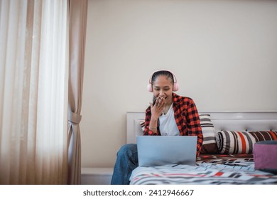 a girl using a headset while watching something using a laptop sitting on a bed