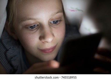 Girl Using Mobile Phone Hiding Under Duvet In Bed At Night