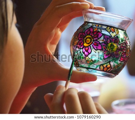 The girl is using a paintbrush painted on a glass.
