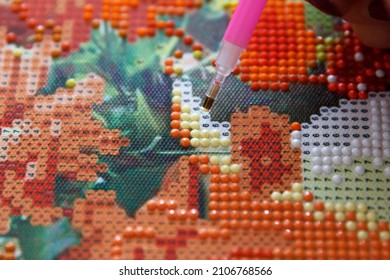 Girl using a pen glues acrylic rhinestones on a diamond 3D painting