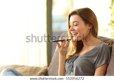 Girl using a smart phone voice recognition on line sitting on a sofa in the living room at home with a warm light and a window in the background