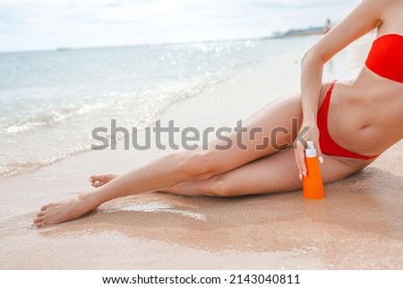 Girl using sunscreen and lying on the beach by the ocean or sea Woman applying sun cream on tanned body to protect her skin. Female holding suntan lotion, moisturizing sunblock on sunny day