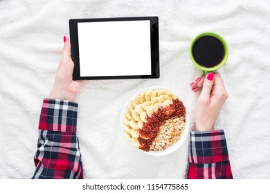 Girl using tablet pc, lying on white crumpled blanket. Women's hands, red manicure, a Cup of coffee or tea, tablet PC close up. Background with copy space for advertisement. Top view