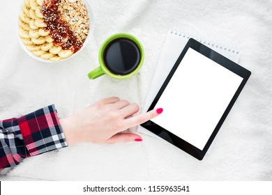 Girl using tablet pc, lying on white crumpled blanket. Women's hands, red manicure, a Cup of coffee or tea, tablet PC close up. Background with copy space for advertisement. Top view