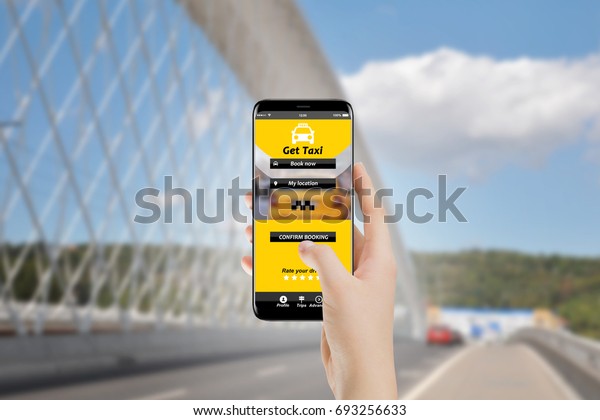 Girl using taxi booking service app on her\
phone, city bridge in\
background