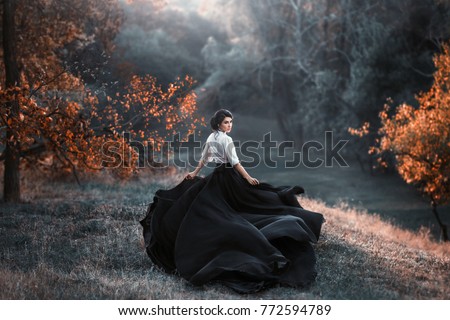 A girl in a vintage dress is running and looking around. The train waving in the wind. Art Photography. Landscape forest, orange trees. Gothic beauty, the dark queen. Wallpaper