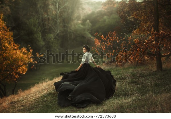 girl in vintage dress running looking around silk\
skirt train fabric waving flying fluttering wind. Artistic\
Photography. Vintage clothes medieval woman queen, mysterious lady\
back. Autumn tree forest