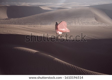 Girl walking across the desert sand dunes with a flowing fabric