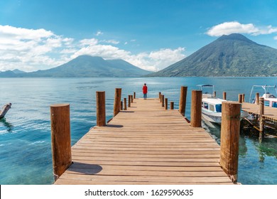 Girl Walking Along Jetty At Lake Atitlán Looking San Pedro Volcano And Atitlán Volcano, Guatemala