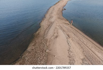 The Girl Is Walking Along The Spit In The Sea. Air View.