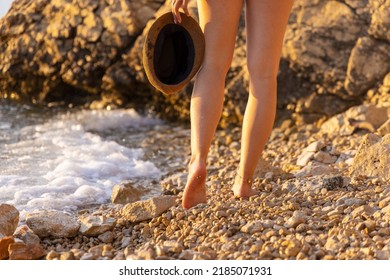 A girl is walking barefoot on a beach with a hat in the hand