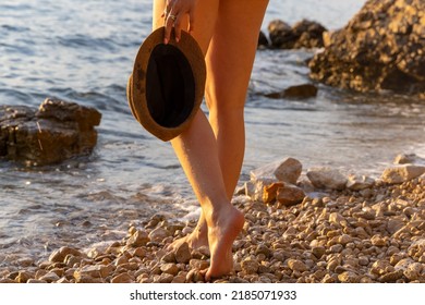 A girl is walking barefoot on a beach with a hat in the hand