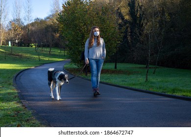 Girl walking the dog at a park with the city at the background with a mask during pandemic - Powered by Shutterstock