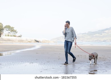 Girl Walking With Dog And Talking On Phone In The Beach.