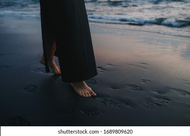 Girl walking in the evening along the sea line on the black sand beach in last sunset lights. Legs close up. Peaceful mind concept and relaxation