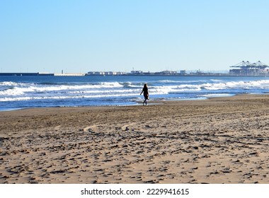 Girl is walking near sea. Young woman walks along sand beach near Mediterranean Sea. Female person walks along coastline of ocean. Waves in Sea. Beach at seaport with Shipping containers in Port. 