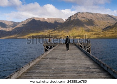 Girl walking on Önundarfjörður Pier and looking at beautiful view over fjord and mountains in Westfjords, Iceland