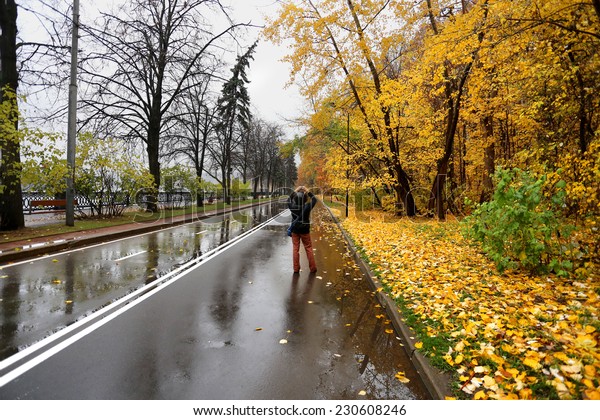 Girl walking on the wet road among an autumn\
forest covered with yellow\
leaves