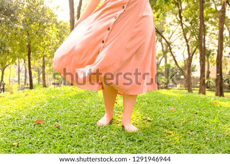 Girl walking in the public garden . she is standing on the green grass field.The wind is blowing. Her orange skirt is fluttering by the wind.